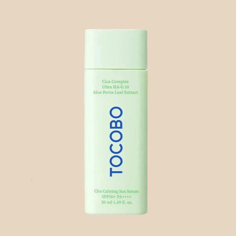A bottle of TocoBo Cica Calming Sun Serum in a pale mint green color, shown against a matching pale beige background with a white cream smear behind it.